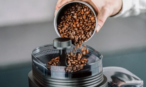 Image d'une personne qui déverse du café dans le moulin en céramique de notre cafetière electrique Aromafresh