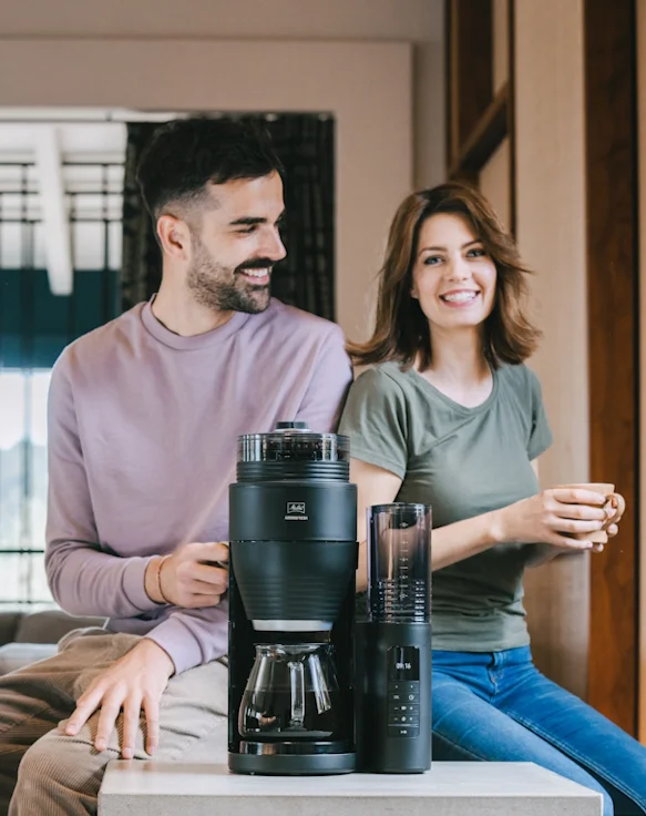 AromaFresh Filterkaffeemaschine, eine Frau und ein Mann sitzen mit einer Tasse in der Hand daneben