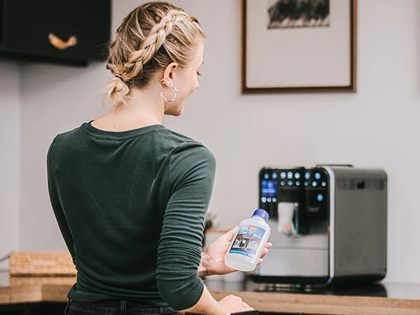 Maschinenpflege für Vollautomaten Frau mit Melitta® Maschinenpflege in der Hand steht vor einem Barista Kaffeevollautomaten