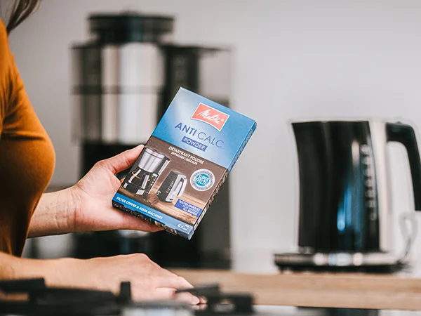 a woman stands with a packet of Melitta descaler for a Melitta kettle and coffee machine