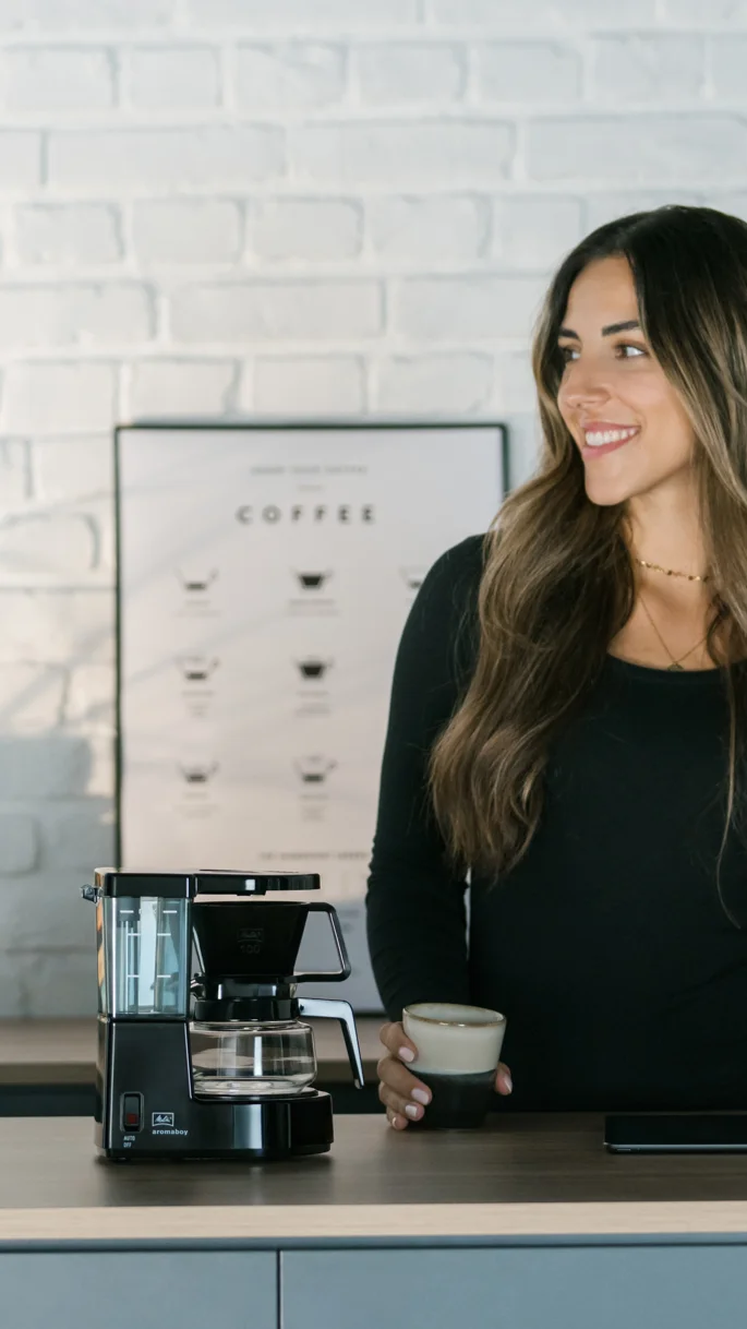 Melitta Aromaboy filterkaffemaskine ved siden af smilende kvinde med kaffekop.