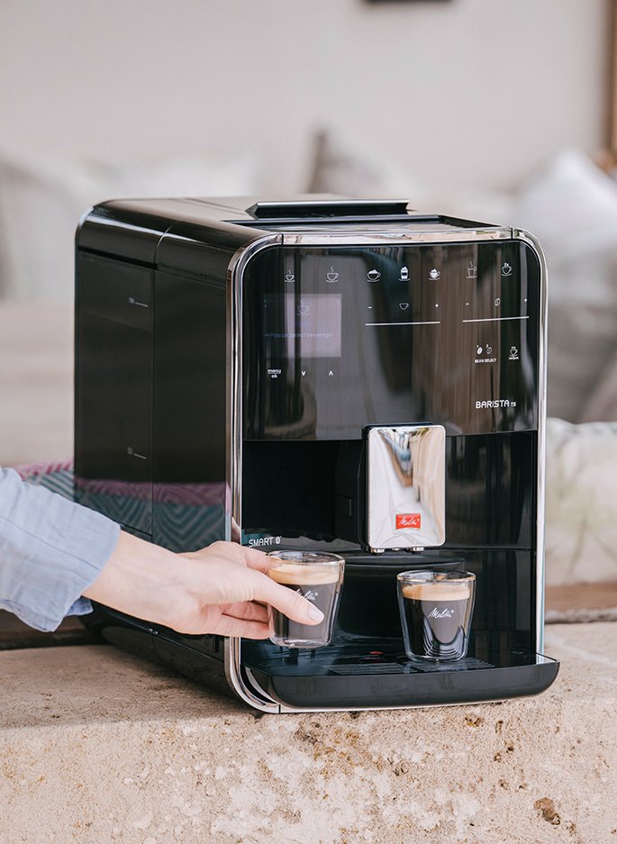 Melitta Barista T Smart mit zwei Espressi, Hand nimmt eine Tasse in gemütlicher Umgebung