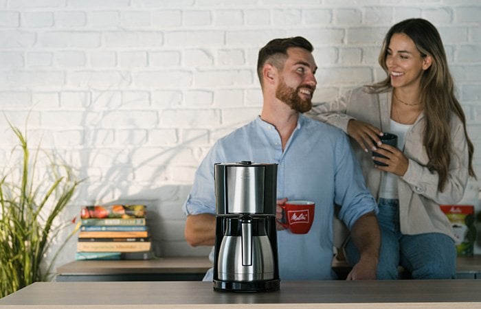 Melitta Enjoy Top Therm filterkaffemaskine foran smilende par med kaffekrus.