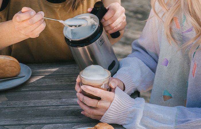 Melitta® Cremio® mælkeskummer med mælkeskum og glas på et udendørs bord