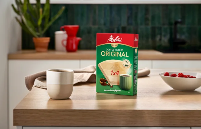 Afbeelding van een kopje en een van onze 1 x 4 koffiefilterdozen op een houten tafel