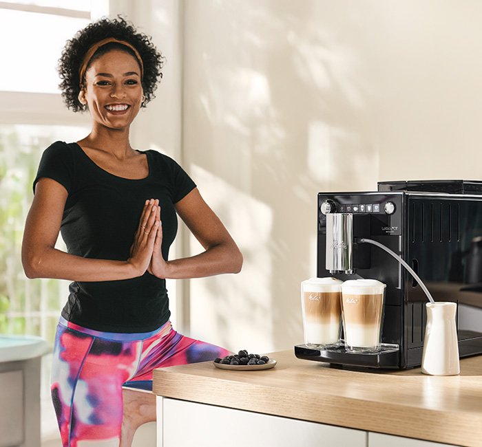 Frau steht neben Vollautomat Latticia® OT, der gerade zwei Latte Macchiato zubereitet hat.