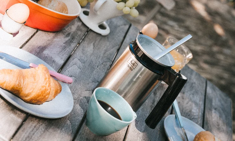 Silver Melitta Cremio milk frother with a cup of coffee and a croissant