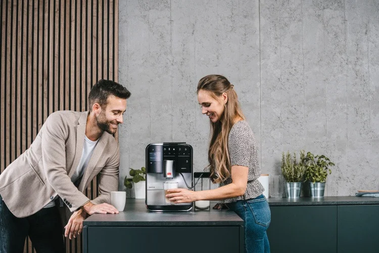 Lächelndes Paar bereitet Kaffee mit einer silbernen Melitta Barista T Smart in moderner Küche zu