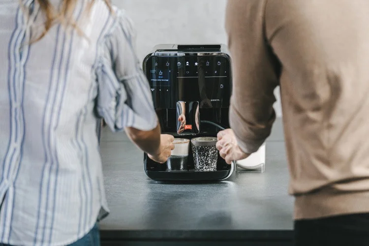 Zwei Personen nehmen Kaffee aus einer schwarzen Melitta Barista T Smart in moderner Küche
