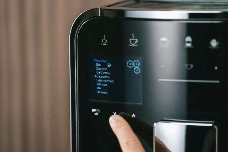 Nahaufnahme des Displays einer schwarzen Melitta Barista T Smart mit Hand bei der Auswahl einer Kaffeespezialität