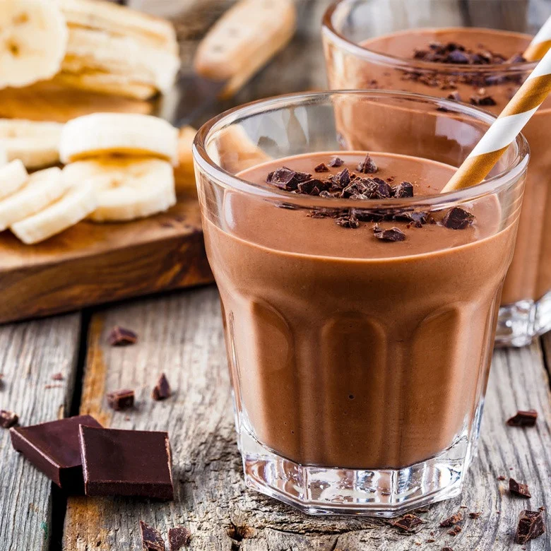 Schoko-Bananen-Smoothie im Glas mit Schokostückchen und Bananenscheiben auf Holztisch