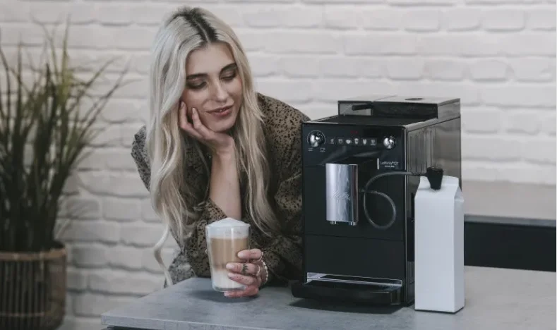 Frau genießt einen Latte Macchiato neben einer schwarzen Melitta Latticia OT mit Milchbehälter