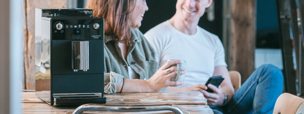 a woman drinks a cup of Melitta coffee with a man next to a Melitta Latticia OT fully automatic machine together
