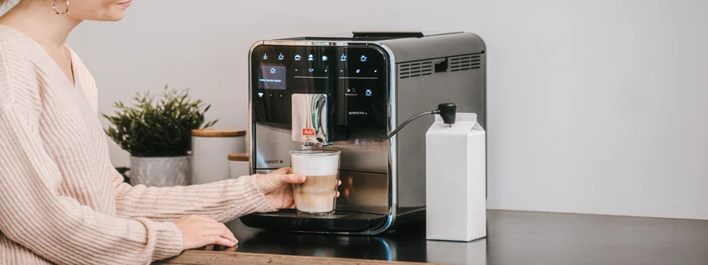 een vrouw haalt een Melitta Latte macchiato onder de uitloop van een Melitta Barista volautomaat vandaan